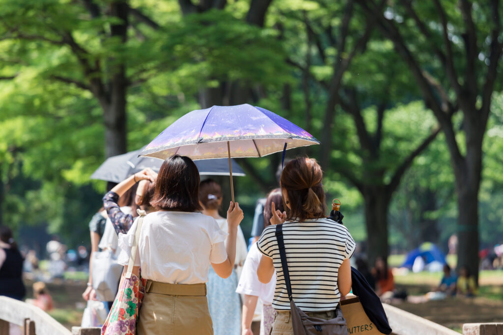 木々の茂る公園の中で相合傘で日傘をさす女性2人
